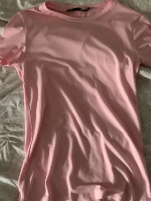 Ljusrosa basic t-shirt - En enkel och stilren ljusrosa t-shirt i mjuk bomull. T-shirten har rund halsringning och korta ärmar, perfekt för en avslappnad look. Passformen är normal och tyget känns skönt mot huden.