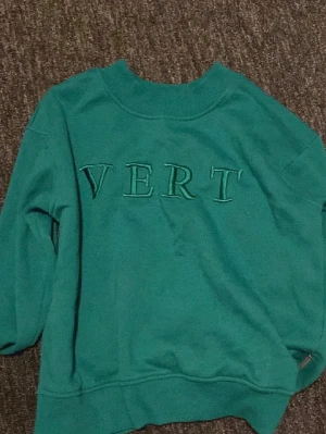 Grön sweatshirt med VERT-tryck - Cool grön sweatshirt med texten 'VERT' broderat framtill. Tröjan har rund halsringning, långa ärmar och ribbade muddar vid ärmslut och nederkant. Perfekt för en avslappnad och trendig look.