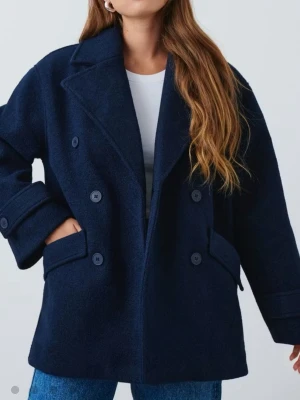 Oversized mörkblå dubbelknäppt ullrock - Snygg mörkblå rock med dubbelknäppning och breda slag. Rocken har två stora fickor framtill och uppvikta ärmslut med knappdetalj. Tillverkad i ett ulligt material som håller dig varm och stilren under kalla dagar.
