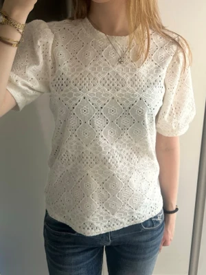 Vit spetsblus med puffärm - Säljer en superfin vit blus med puffärmar och vackert spetsmönster. Blusen har rund halsringning och är tillverkad i ett luftigt material som känns perfekt för varmare dagar. Passformen är normal och toppen har fina detaljer i spets över hela plagget.