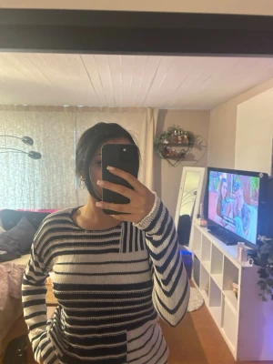 Randig stickad tröja i blått och vitt - Säljer en stickad tröja med breda blå och vita ränder. Tröjan har lång ärm och rund halsringning, samt ett coolt rutmönster på bröstet. Perfekt för dig som gillar en avslappnad och trendig look. Materialet är mjukt och bekvämt.