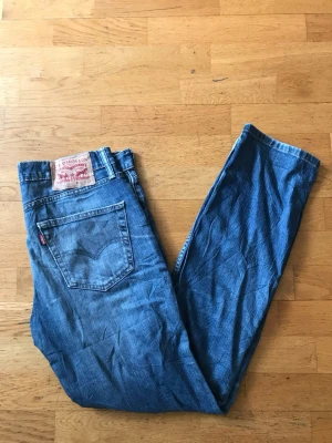 Levi's 511 blå jeans herr - Säljer ett par klassiska blå Levi's 511 jeans med rak passform och normal midja. Jeansen har fem fickor, Levi's röda etikett på bakfickan och patch med logga bak i midjan. Tillverkade i slitstark denim, perfekta för en avslappnad stil.