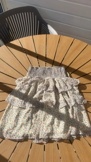 Blommig volangkjol från Vila - Supersöt kort kjol från Vila med blommigt mönster i pastellfärger. Kjolen har bred smock i midjan och flera lager volanger🌸