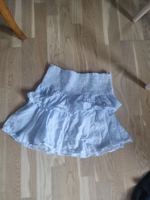 Vitblå topp från Gina Tricot - Supersöt vitblå topp från Gina Tricot med bred smock och dubbla volanger. Toppen är gjord i ett tunt, luftigt tyg som ger en flowy känsla. Är en topp men går att använda som kjol. Strl 170