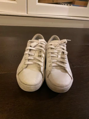  Lacoste sneakers vitt läder - Säljer ett par klassiska vita sneakers från Lacoste i läder med den ikoniska gröna krokodilloggan på sidan. Skorna har vita snören, låg profil och diskret design som passar till det mesta. Perfekta för dig som gillar stilrena och tidlösa sneakers.