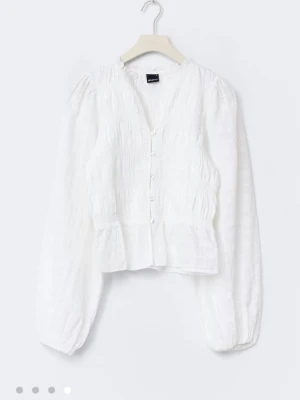 Vit blus med knappar från Gina Tricot - Helt ny blus helt oanvänd även prislappen kvar. Blusen är från Gina Tricot och har en långärmad design och smockdetaljer över bröstet. Blusen har v-ringning, knappar framtill och lätt volang nedtill. Tillverkad i ett tunt, luftigt material💕