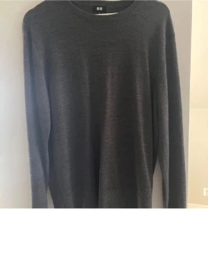 Crewneck 100% merinoull  - En stilren mörkgrå stickad tröja med rund halsringning och långa ärmar. Tröjan är tunnstickad och har en klassisk, rak passform som funkar till det mesta. Perfekt basplagg i garderoben.