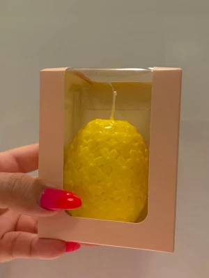 Gul blomformad ljusdekoration - Säljer ett gult ljus i form av ett ägg täckt med små blommor. Ljuset kommer i en söt presentförpackning med fönster. Perfekt som dekoration till påsk eller för att lysa upp rummet med en färgglad detalj.