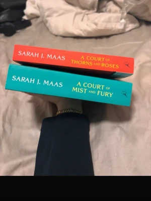 A Court of Thorns and Roses & Mist and Fury - Två populära fantasyböcker av Sarah J. Maas: 'A Court of Thorns and Roses' med röd framsida och 'A Court of Mist and Fury' med turkos framsida. Perfekta för dig som gillar spännande och romantiska berättelser. Mjuka pärmar, engelska. Har inte använt 