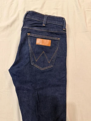 Mörkblå jeans från Wrangler - Ett par mörkblå jeans från Wrangler. Jeansen har en klassisk design med fickor, bälteshällor och en dragkedja med knappstängning. Säljs till 92% lägre pris än originalpriset. W: 29 / L: 32