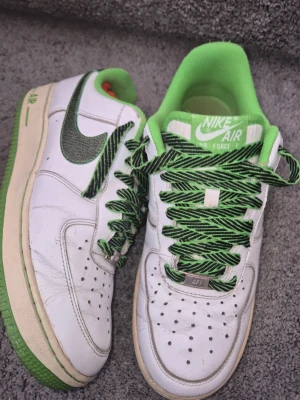 Nike Air Force 1 Low Candy Green Apple - Nike Air Force 1 Low Candy Green Apple  Vita lädersneakers med gröna detaljer, grön sula och grönt innerfoder. Utrustade med mönstrade svart-gröna snören och klassisk Nike Swoosh i matchande färger. Perforerad tåbox för ventilation och den klassiska Air Force 1-silhuetten. Använda med mindre creases (rynkor), annars i bra skick..