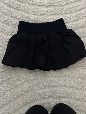 Svart volangskort från H&M - Supersnygg svart skort från H&M med bred resår i midjan och volangig kjoldel. Perfekt för dig som gillar en sportig men ändå söt look. Tillverkad i mjukt och stretchigt material som är bekvämt hela dagen.