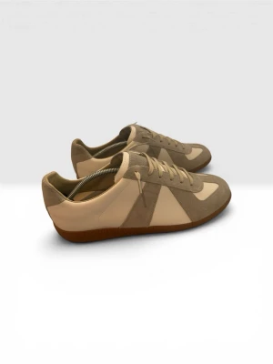 Mason Margiela Gats - Snygga sneakers i beige och vitt med ovandel i mocka och släta skinnpaneler. Klassisk låg modell med gummisula och neutrala färger som passar till det mesta. Skorna har snörning och en stilren design inspirerad av retro-träningsskor.