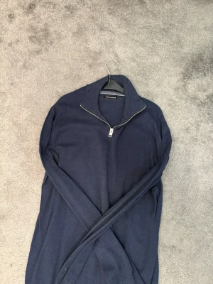 Mörkblå halvzip från Jack & Jones - Mörkblå stickad tröja från Jack & Jones med halvzip och hög krage. Tröjan har långa ärmar och ribbade muddar vid ärmslut och nederkant. Perfekt för lager på lager och enkel att matcha med jeans eller chinos.