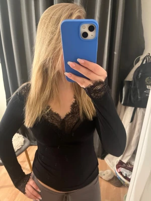 Svart intimissmi topp med spets - Snygg svart långärmad topp med v-ringning och spetsdetaljer vid halsringning och ärmslut. Figurnära passform som ger en elegant look. Perfekt att styla med jeans eller kjol för en trendig outfit.