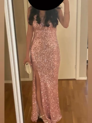 Rosa glittrig långklänning med slits - Supersnygg rosa långklänning täckt av paljetter med smala axelband och snörning i ryggen. Klänningen har en hög slits framtill och figurnära passform som ger en elegant siluett. Perfekt för bal eller festliga tillfällen. Köpt på L&S butiken i Göteborg. Använt 1 gång, klänningen är som ny.  Ny pris 2500:-
