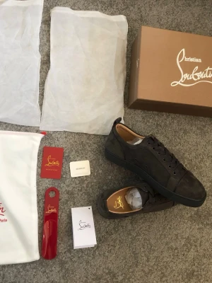 Gråa sneakers från Louboutin - Snygga gråa sneakers från Christian Louboutin i mocka med klassisk låg siluett och gråa snören. Skorna har diskreta detaljer och en röd sula. Perfekta för dig som gillar exklusiv och stilren design. Säljer mina skor för att de inte passar, har testat de en gång annars helt nya. Box och tillbehör tillkommer. (Rep)