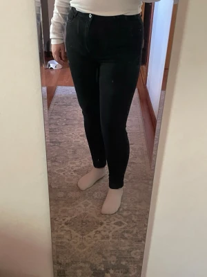 Svarta skinny jeans med hög midja - Säljer ett par svarta skinny jeans med hög midja och klassisk femficksdesign. Jeansen har smal passform hela vägen ner och stängs med knapp och dragkedja. Materialet är stretchigt för extra komfort och de är perfekta till en enkel vardagslook. Längden är 32 men jag har dem uppvikta till 30 så de passar båda.
