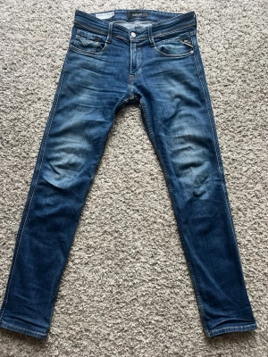 Blå slim fit jeans från Replay - Snygga blå slim fit jeans från Replay med klassisk femficksdesign och diskreta slitningar framtill. Jeansen har normal midja, dragkedjegylf och är tillverkade i stretchig denim för en bekväm passform. Knappt använda. 