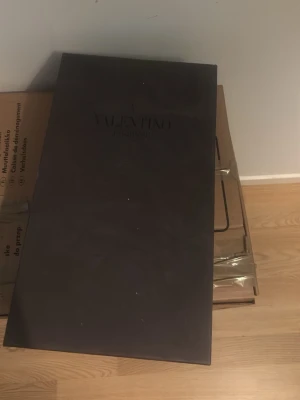 Stor svart presentbox från Valentino - Säljer en stor svart presentbox från Valentino Garavani. Boxen har en elegant och stilren design med diskret logga på locket. Perfekt för att förvara eller ge bort exklusiva accessoarer eller väskor. Materialet är hård kartong med matt finish. 