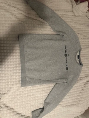 Grå sweatshirt från Sail Racing - Snygg grå sweatshirt från Sail Racing med svart logga tryckt på bröstet. Tröjan har rund halsringning, långa ärmar och är gjord i mjukt sweatshirtmaterial. Perfekt för en avslappnad och sportig stil. Den är 170 men det kan vara typ 150-165 för att andvänd