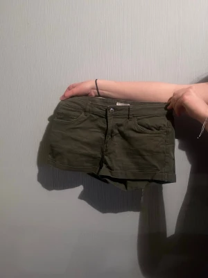 Olivgröna shorts med fickor - Snygga olivgröna shorts med klassisk femficksdesign och knappstängning. De har bälteshällor och är tillverkade i ett mjukt bomullsmaterial. 