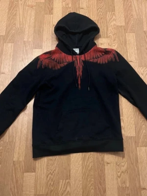Marcelo burlon - Snygg svart hoodie från Marcelo Burlon med en unik röd fågeldesign över axlar och bröst. Hoodien har huva med dragsko och en klassisk magficka. Perfekt för dig som vill sticka ut med en cool streetwear-look.