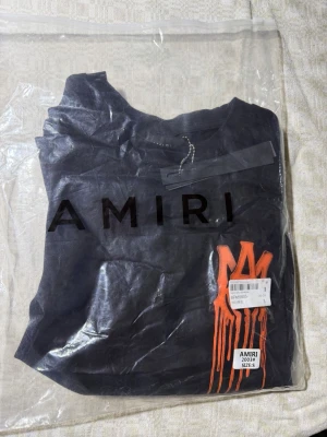 Svart AMIRI t-shirt - Cool svart t-shirt från AMIRI med ett orange, droppande logotryck på bröstet. Klassisk passform med rund hals och korta ärmar. Oanvänd bara testat på en gång. Allt som jag säljer blir tagen hand om innan den skickas ut så du får så bra resultat som möjligt.