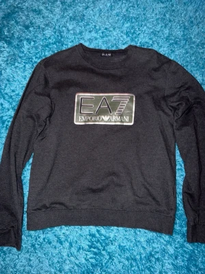 Emporio Armani tröja - Snygg mörkgrå sweatshirt från EA7 Emporio armani. Tröjan har rund halsringning och långa ärmar. Storlek L men sitter som S.