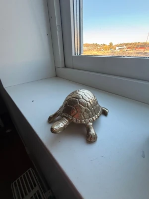 Dekorativ guldfärgad sköldpadda - Säljer en dekorativ sköldpadda i guldfärgad metall. Sköldpaddan har en detaljerad skalstruktur och står stadigt på fyra ben. Perfekt som prydnad till fönsterbrädan eller hyllan för dig som gillar unika inredningsdetaljer.