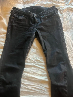 Svarta true religon jeans  - Säljer ett par svarta jeans från true religon. Materialet är mjukt och stretchigt för extra komfort. Perfekta till en avslappnad stil. De har varit ett hål som blivit sytt och lite nedtrampade längst ned annars inga defekter, skriv innan köp. 