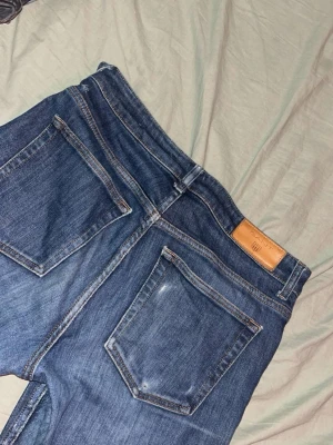 Blå raka jeans från GANT - Säljer ett par klassiska blå jeans från Gant med raka ben och femficksmodell. Jeansen har en snygg tvätt, kontrastsömmar och läderpatch bak i midjan. Perfekta för en avslappnad och stilren look.