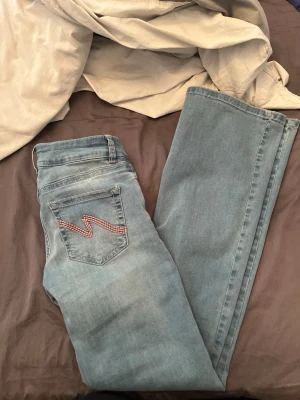 Ljusblå bootcut jeans från Nelly  - Säljer ett par ljusblå bootcut jeans från Nelly med snygg broderad detalj på bakfickan. Jeansen har normal midja och är tillverkade i mjukt denimtyg som ger en avslappnad look.