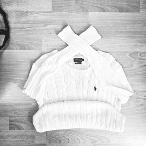 Vit kabelstickad tröja Polo Ralph Lauren - Klassisk vit cable knit tröja från Polo Ralph Lauren med fin flätstickning över hela, ribbad nederkant och ärmar samt det ikoniska broderade ponylogot på bröstet. Tillverkad i mjuk Pima Cotton. Passform: Damstorlek – sitter som en normal M (bra och vanlig passform, inte för tight eller oversized). Mått (platt): Axelbredd: ca 48–50 cm Pit to pit: ca 51–53 cm Längd: ca 66–68 cm Skick: Mycket bra skick – har använts ett fåtal gånger och är fortfarande i fint skick. Inga problem eller defekter. Pack
