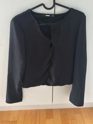 Svart långärmad topp från Bik Bok - Stilren svart långärmad topp från Bik Bok med croppad passform och snygg twistad detalj framtill. Tillverkad i ett mjukt, lätt material som ger en clean look. Perfekt att matcha med jeans eller kjol.