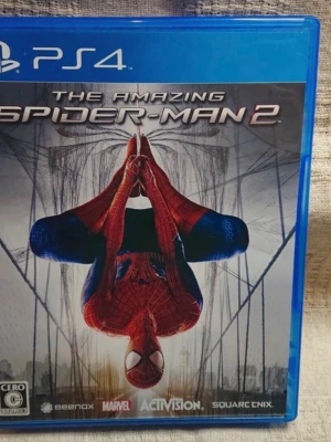 The Amazing Spider-Man 2 PS4 spel - The Amazing Spider-Man 2 till PS4 är ett actionäventyrsspel där du spelar som Marvels ikoniska superhjälte. Omslaget är blått med Spider-Man i röd och blå dräkt, hängandes upp och ner i ett spindelnät. Utvecklat av Beenox och utgivet av Activision.