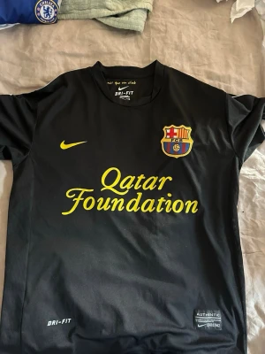 Svart FC Barcelona o Chelsea matchtröja Nike - Säljer en svart FC Barcelona matchtröja från Nike med Qatar Foundation-tryck i gult och klubbmärke på bröstet. Tröjan har Dri-Fit-material som andas och korta ärmar. Perfekt för dig som älskar fotboll och vill ha en snygg supportertröja. A1 kopior men väldigt bra skick! Storlek M-L