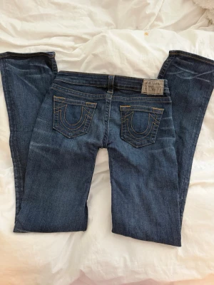 True Religion bootcut jeans - Säljer ett par mörkblå jeans från True Religion med bootcut-modell och ikoniska kontrastsömmar på bakfickorna. Jeansen är low waist och jag har själv sytt om dem till det! Använd ett fåtal gånger, skulle säga max 10 ❤️de är rätt så långa i benen, passar någon som är 165-175 skulle jag säga 