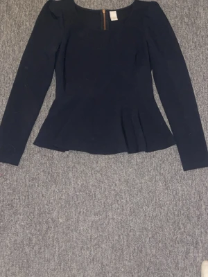 Marinblå  peplumblus från vila - Marin  peplumblus från vila  med rund halsringning och långa ärmar. Blusen har en figurnära passform upptill och en utställd nederdel som.. Perfekt till jeans eller kjol💝💝