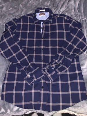 Mörkblå rutig skjorta från Esprit - Snygg mörkblå skjorta från Esprit med stora beigea rutor. Skjortan har klassisk krage, långa ärmar och knäppning framtill. Tillverkad i ett mjukt och bekvämt material som passar perfekt till lager på lager under vintern. Stilsäker och enkel att matcha.