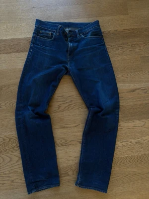 Mörkblå jeans från Carhartt - Snygga mörkblå Carhartt Pontiac pants med klassisk femficksdesign och raka ben. Jeansen har en diskret logga på bakfickan och är tillverkade i slitstark denim. Perfekta för en avslappnad och stilren look.