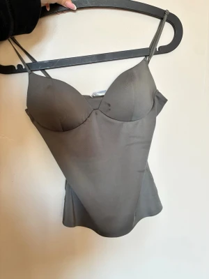 Grå satin bustier från Zara - Snygg grå bustier-top från Zara i satinliknande material med tunna justerbara axelband och den har en fläck på ena bröstet men har ej tvättat den så det kan vara så att den går bort. 