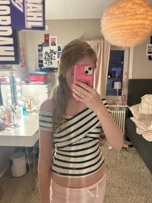 Randig offshoulder topp i ribbad bomull - Säljer en snygg offshoulder topp med marinblå och vita ränder. Toppen är ribbad och har en tight passform med omlott-detalj framtill. Perfekt för dig som gillar trendiga och bekväma plagg. Materialet känns mjukt och stretchigt.