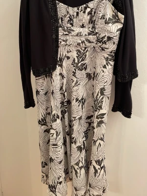 Svartvit axelbandslös klänning - Säljer en snygg axelbandslös klänning i svartvitt blommönster. Klänningen har markerad midja och ett elegant fall. Materialet känns mjukt och följsamt, perfekt för dig som gillar stilrena och trendiga plagg med unik design.