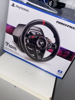 Thrustmaster T128 ratt och pedaler - Säljer en Thrustmaster T128 racerratt med pedaler för PlayStation. Ratten har force feedback, svart design med röda detaljer och flera knappar för spelkontroll. Perfekt för racing och simracing på konsol. Kompatibel med PlayStation.