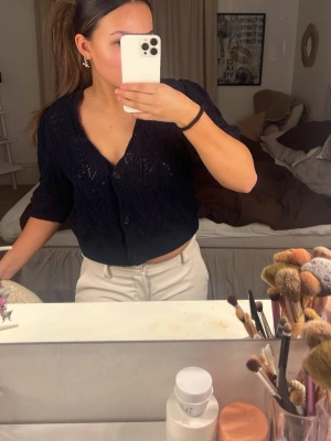 Mörkblå kortärmad kofta - Snygg mörkblå kofta med korta ärmar och djup v-ringning. Koftan har ett fint stickat mönster och stängs med stora knappar framtill. Köpt på Sellpy 