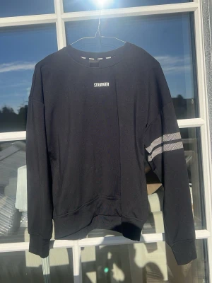Svart sweatshirt från Stronger - Skön svart sweatshirt från Stronger med vita ränder, super bra för för gym eller träning med sportig outfit. Jag själv har bara haft den till vardags och älskar den men jag har 2 därför säljer jag en. 