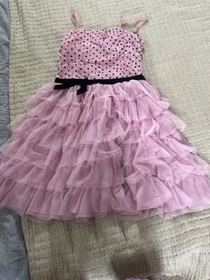 Cool rosa volangklänning - Supersöt rosa volangklänning med tunna axelband. Överdelen har svarta prickar, svart rosett i midjan och stretch på övre ryggen. Nederdelen är i flera fluffiga lager med volanger. Den är ifrån Kids by Lindex i storlek 170 men passar mig med xs o ibland s. Inga defekter💗🤍