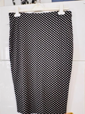 Svartvit prickig kjol från Vince Camuto - Säljer en svartvit prickig kjol från Vince Camuto. Kjolen har en rak, smal passform och är knälång. Tillverkad i ett mjukt och stretchigt material som sitter snyggt på kroppen. Perfekt för dig som gillar klassiska mönster med en modern twist.