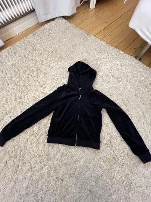 Mörkblå juicy hoodie med dragkedja - Mysig mörkblå hoodie i velour med dragkedja framtill och kängurufickor. Tröjan har huva och ribbade muddar vid ärmslut och nederkant. Perfekt för en chill och avslappnad stil.